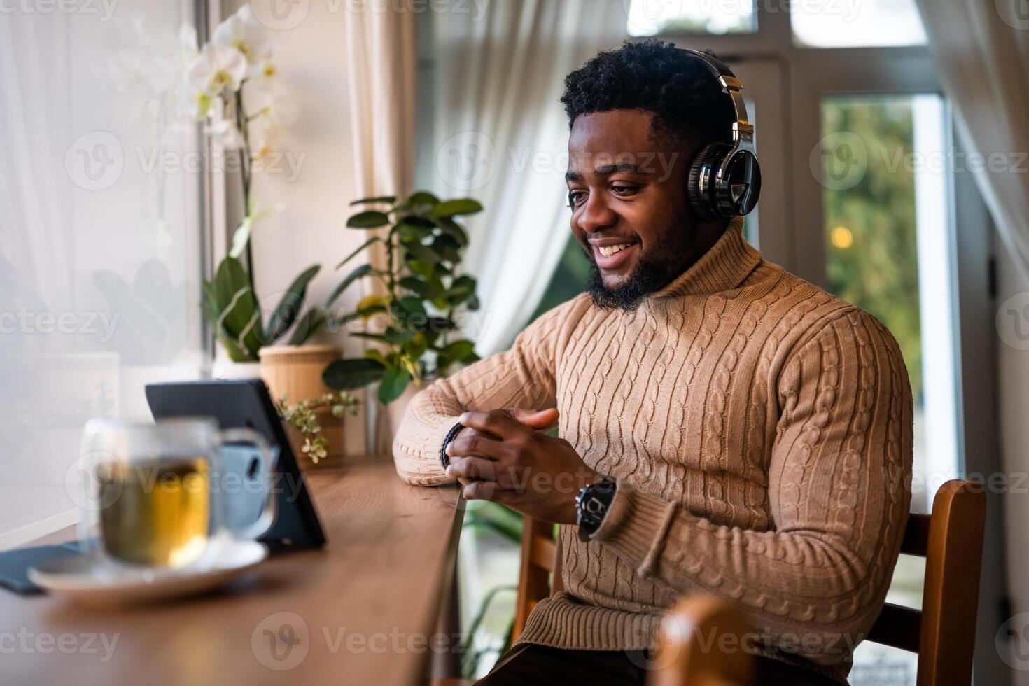 Happy and confident African American man using headphones and digital tablet to work remotely while sitting at table in cafe. photo