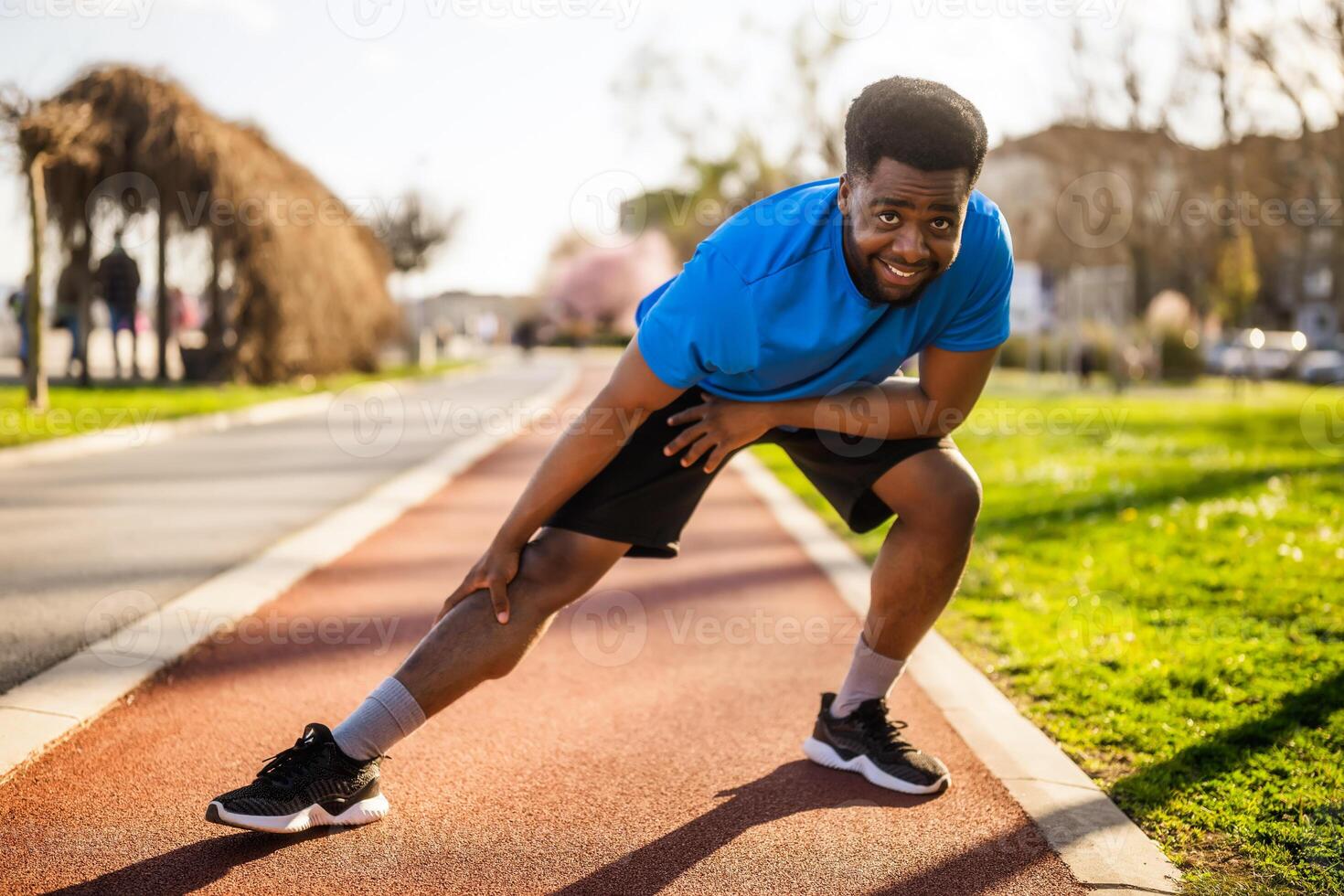Confident young African man stretching his body at running track, preparing for challenging workout outdoor. photo