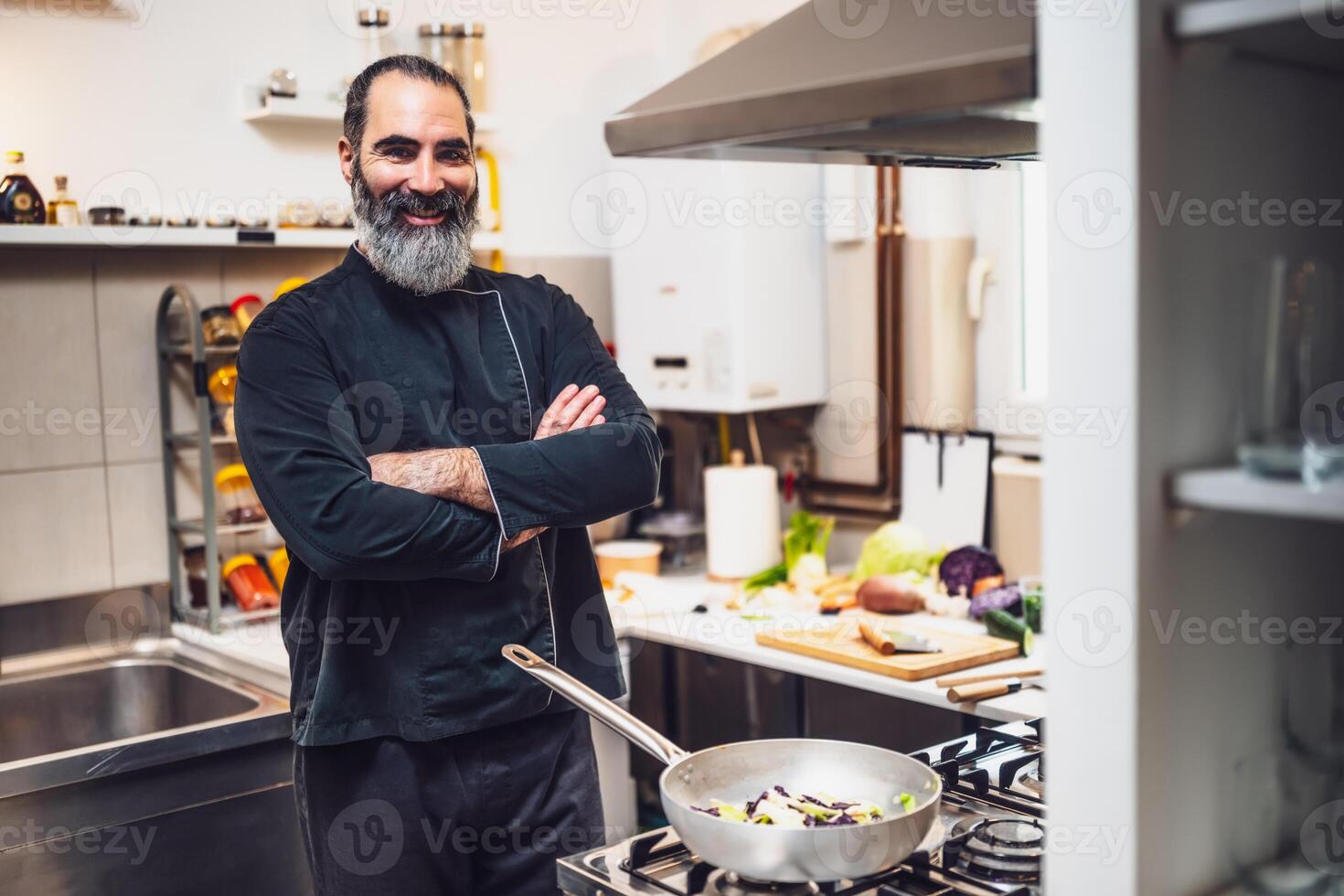 Portrait of confident male chef with arms crossed in apron standing in professional kitchen looking at camera with confidence and pride in his culinary craft. photo