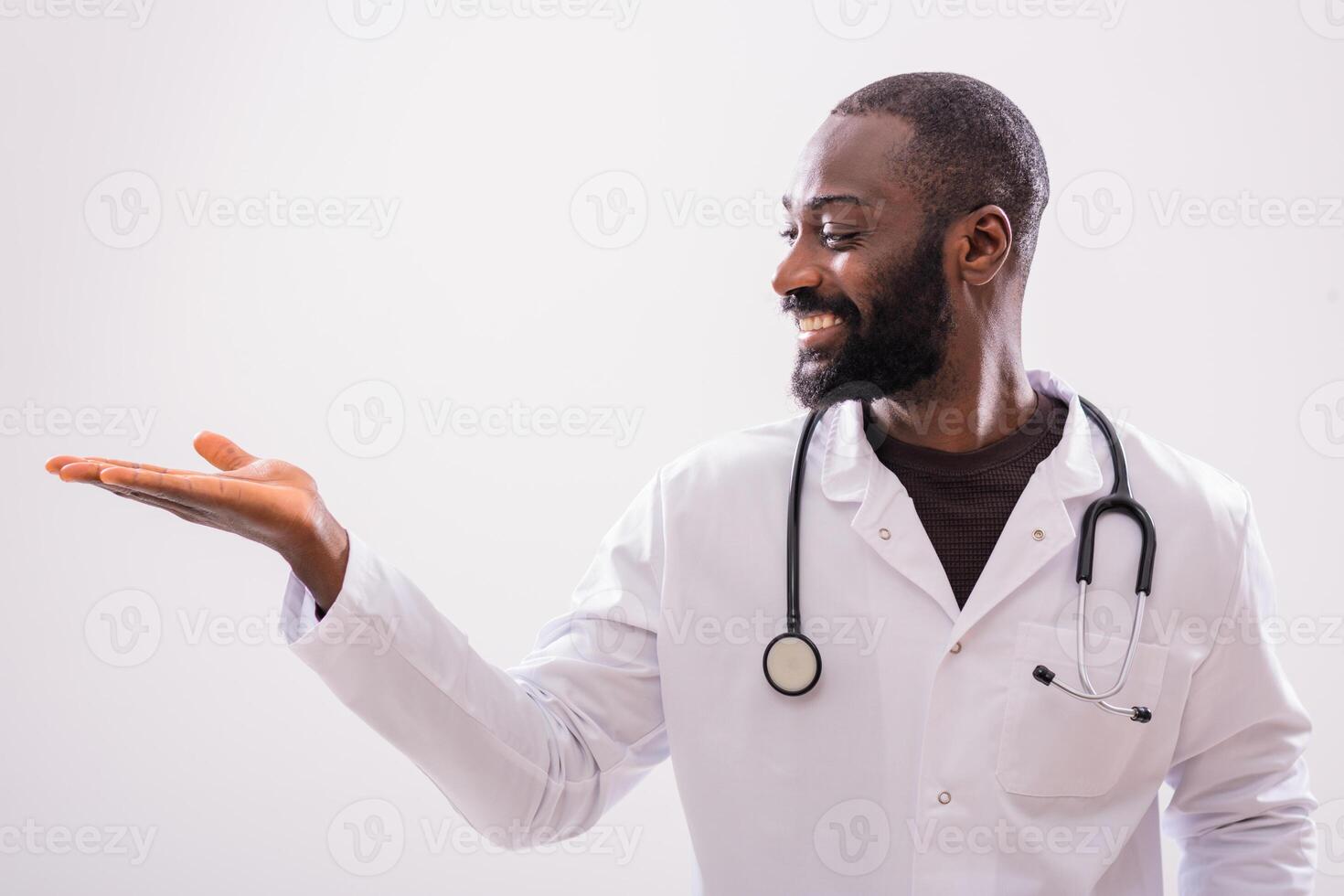 Portrait of cheerful black doctor who is showing palm of hand on gray background. Copy space for your text or advertisement. photo