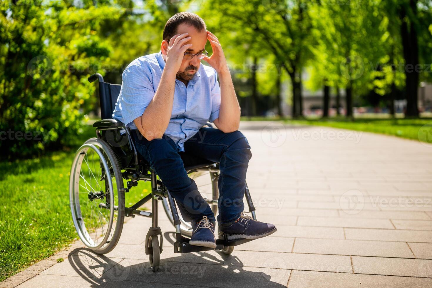 Worried paraplegic man sitting alone in wheelchair outdoor, showing signs of deep thought and sadness. photo