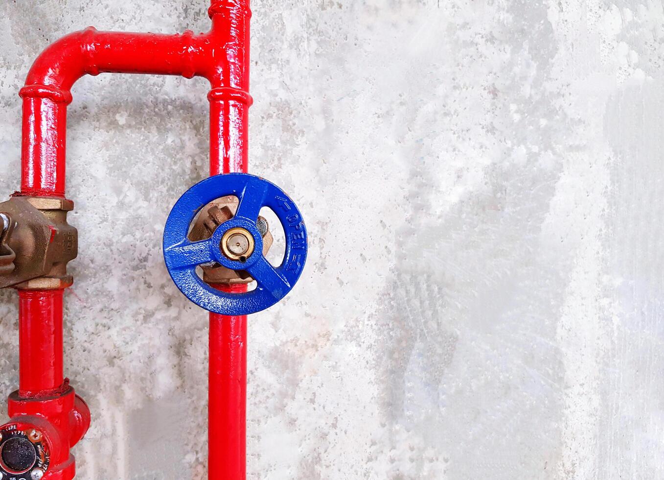 Red water pipe line with blue water valves installed on gray rough concrete wall background with copy space. Industrial and System installation concept. photo