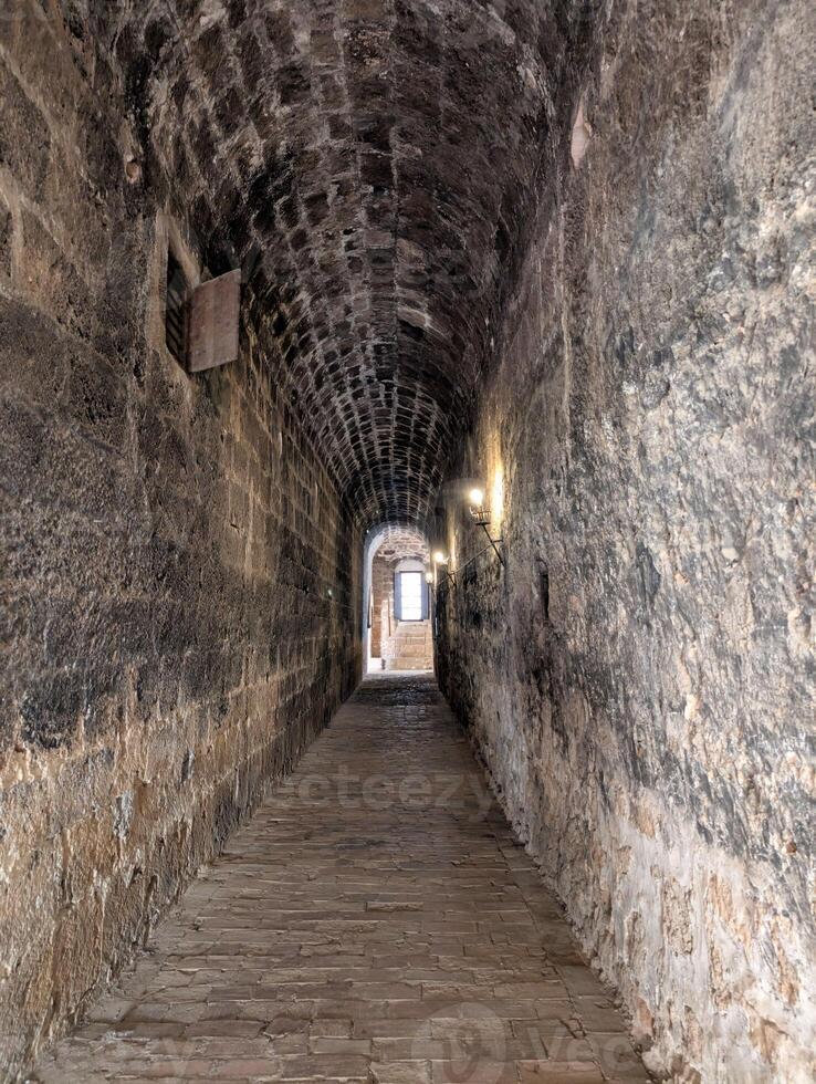 Historic stone corridor featuring aged walls and cobblestone floor, illuminated by soft lights, inviting exploration in a quiet location photo