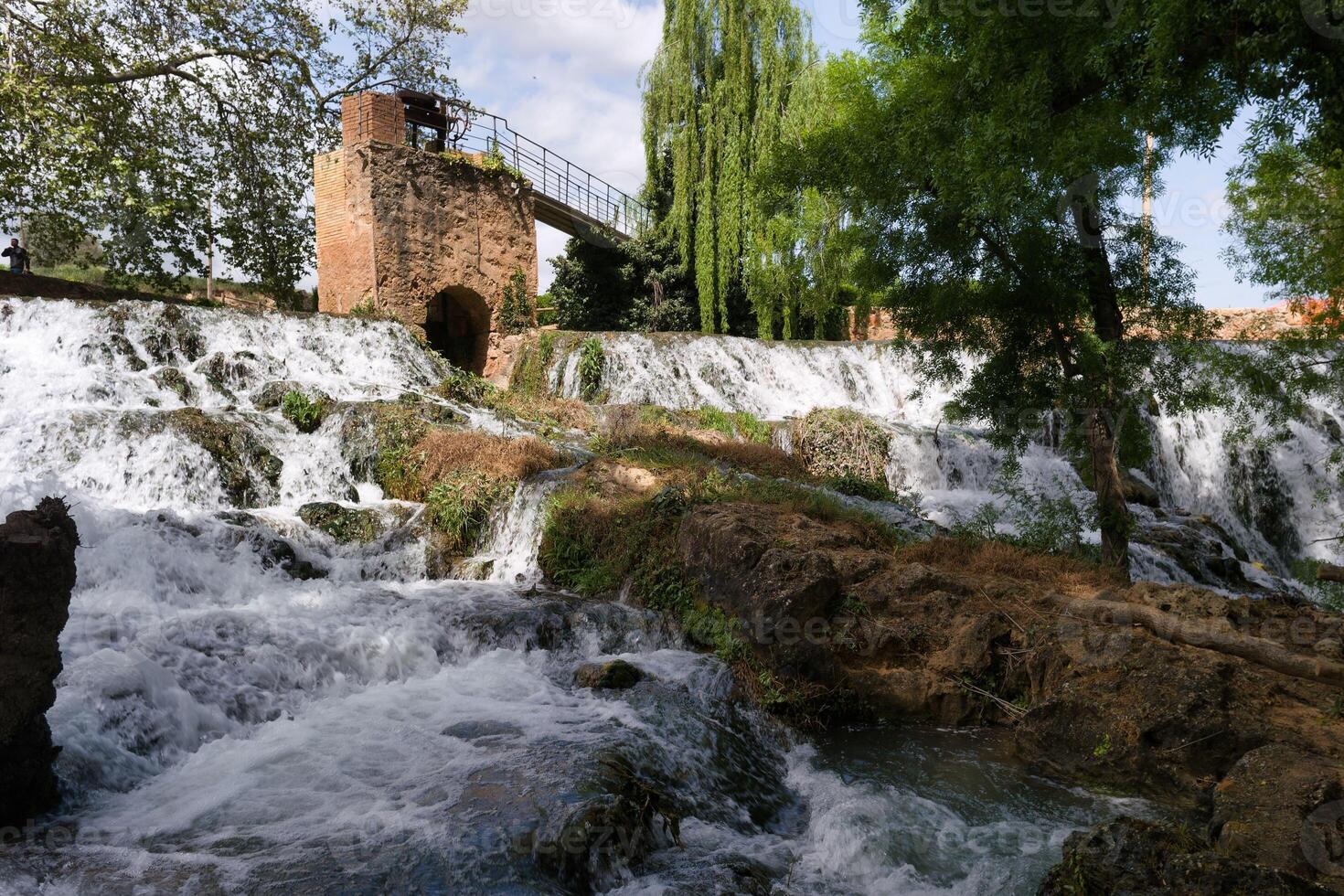 Beautiful cascading waterfall in a serene natural setting surrounded by lush greenery and historical ruins photo