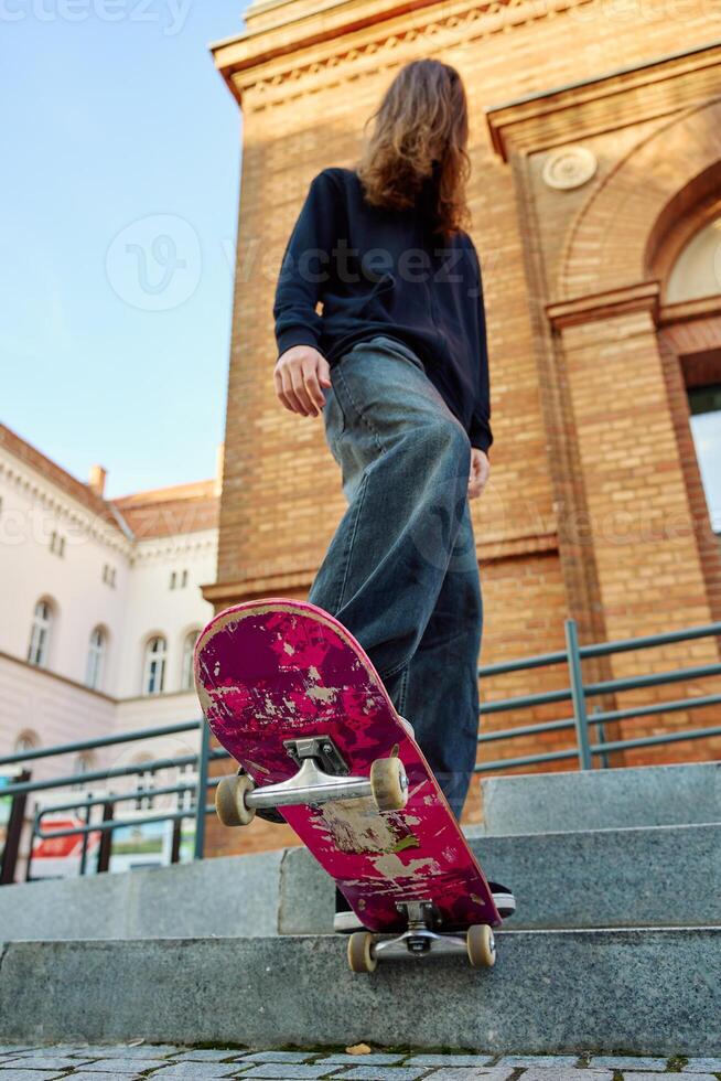 Low angle view of skateboarder balancing on pink skateboard. Close up of underside of deck and wheels of skateboard on stairs at city street photo