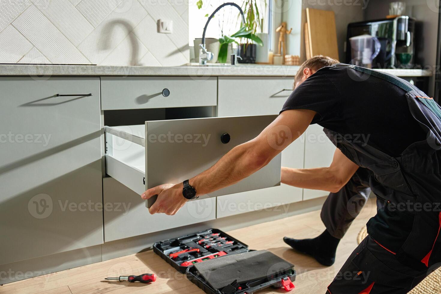 Handyman installing and adjusting drawer slide mechanism in contemporary kitchen. Furniture installation photo