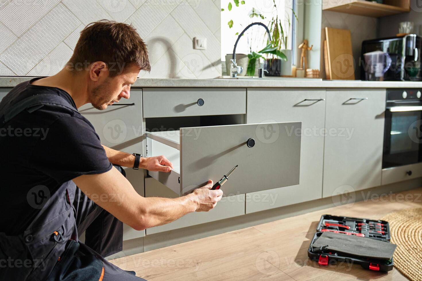 Man assembling kitchen drawer in modern cabinet using screwdriver photo