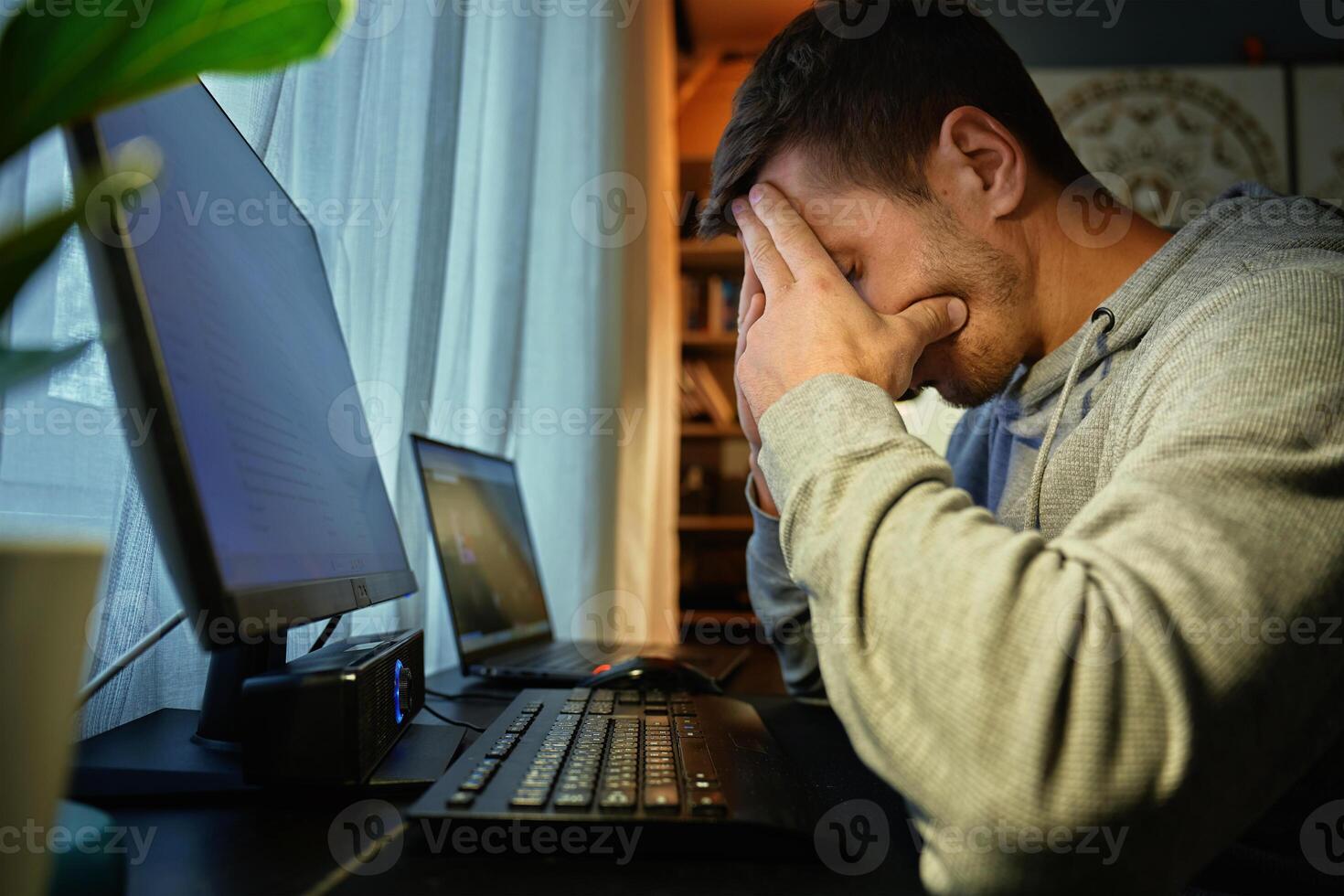 Exhausted man at home office with hands on face after long work hours photo
