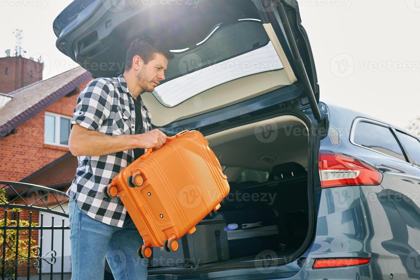 Man loading suitcase into car trunk, Packing luggage for travel photo