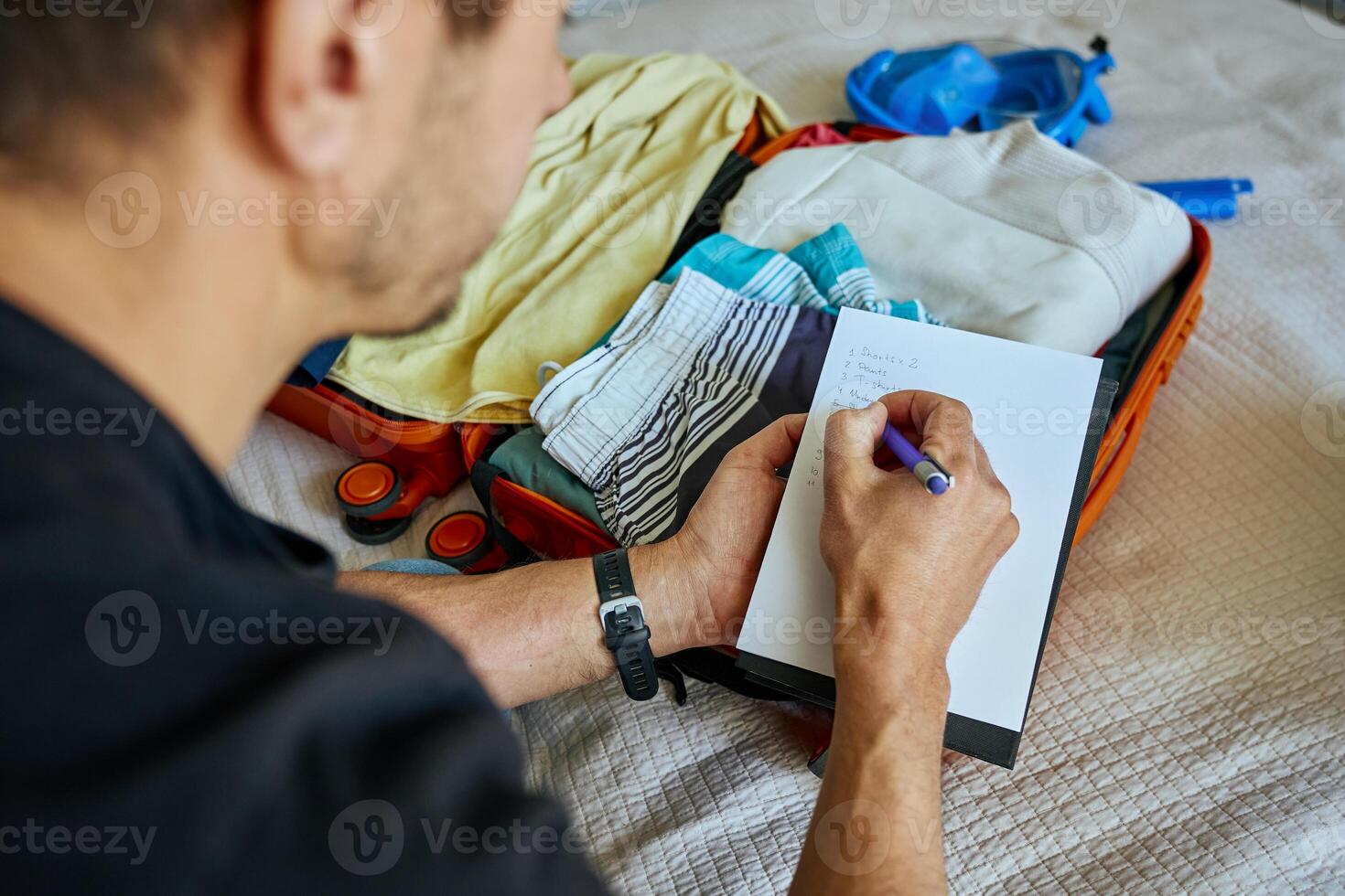 Man packing suitcase and writing travel checklist photo