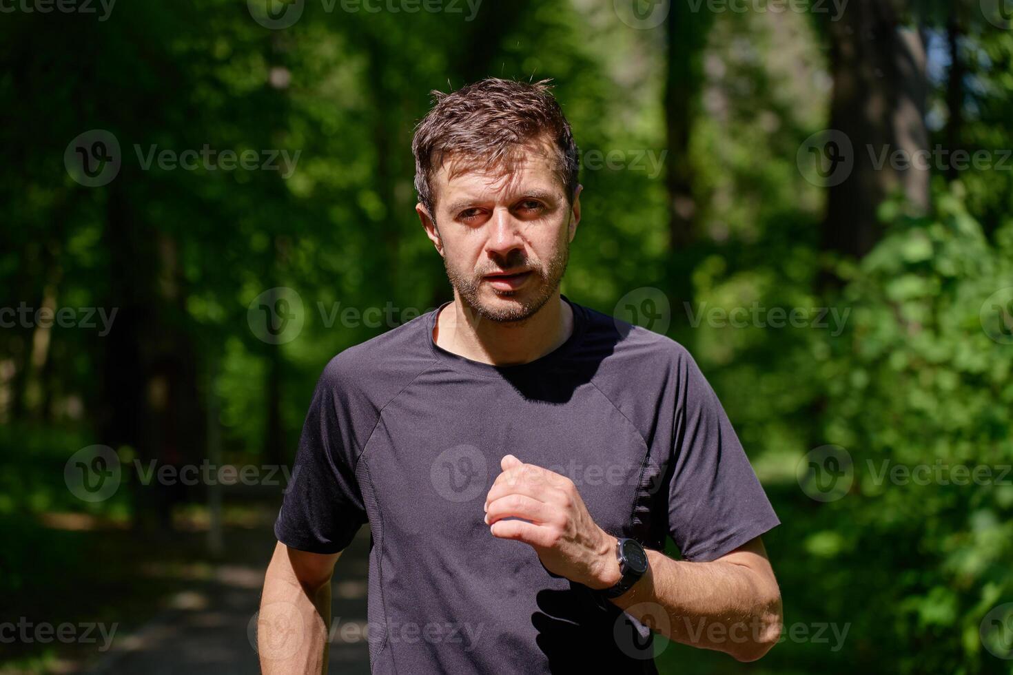 Man running on trail through green park in summer day. Outdoor cardio training in nature photo