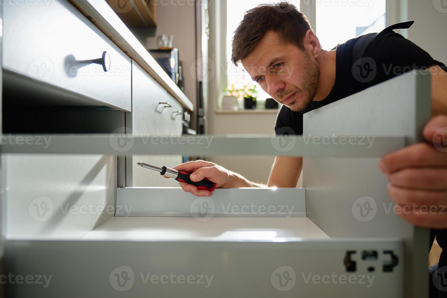 MaleCarpenter installing and adjusting drawer front in kitchen cabinet c photo