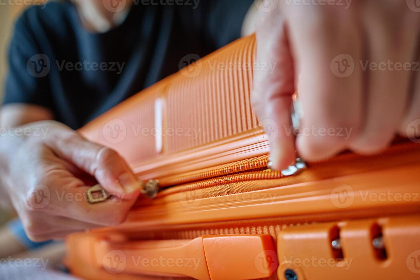 Close-up of hands zipping orange suitcase before trip photo