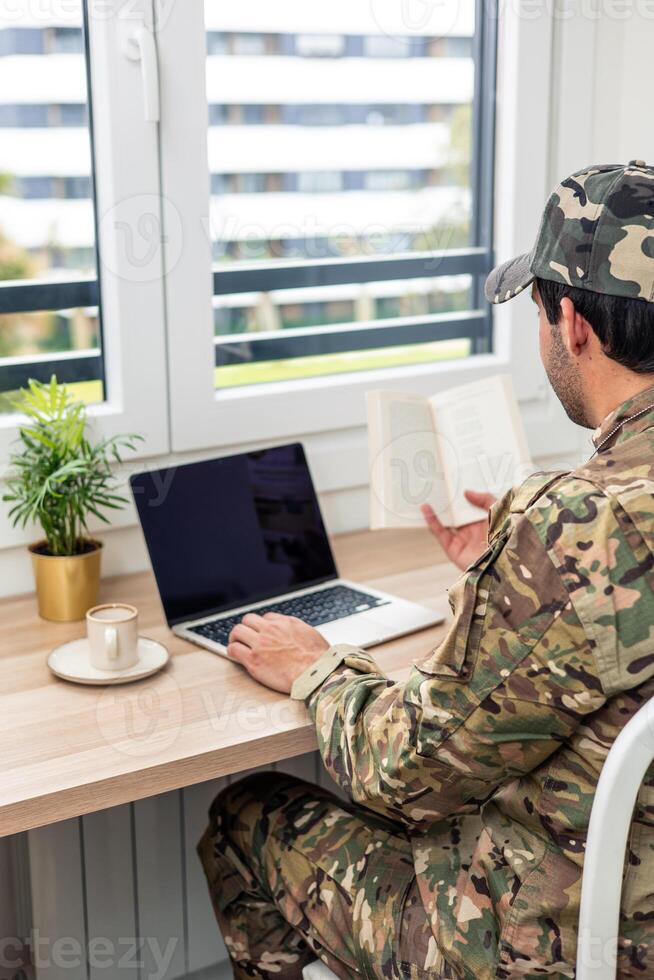 vertical Soldier studying using laptop and book at home photo