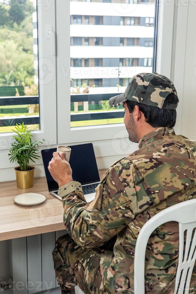 vertical Soldier drinking coffee working from home using laptop photo