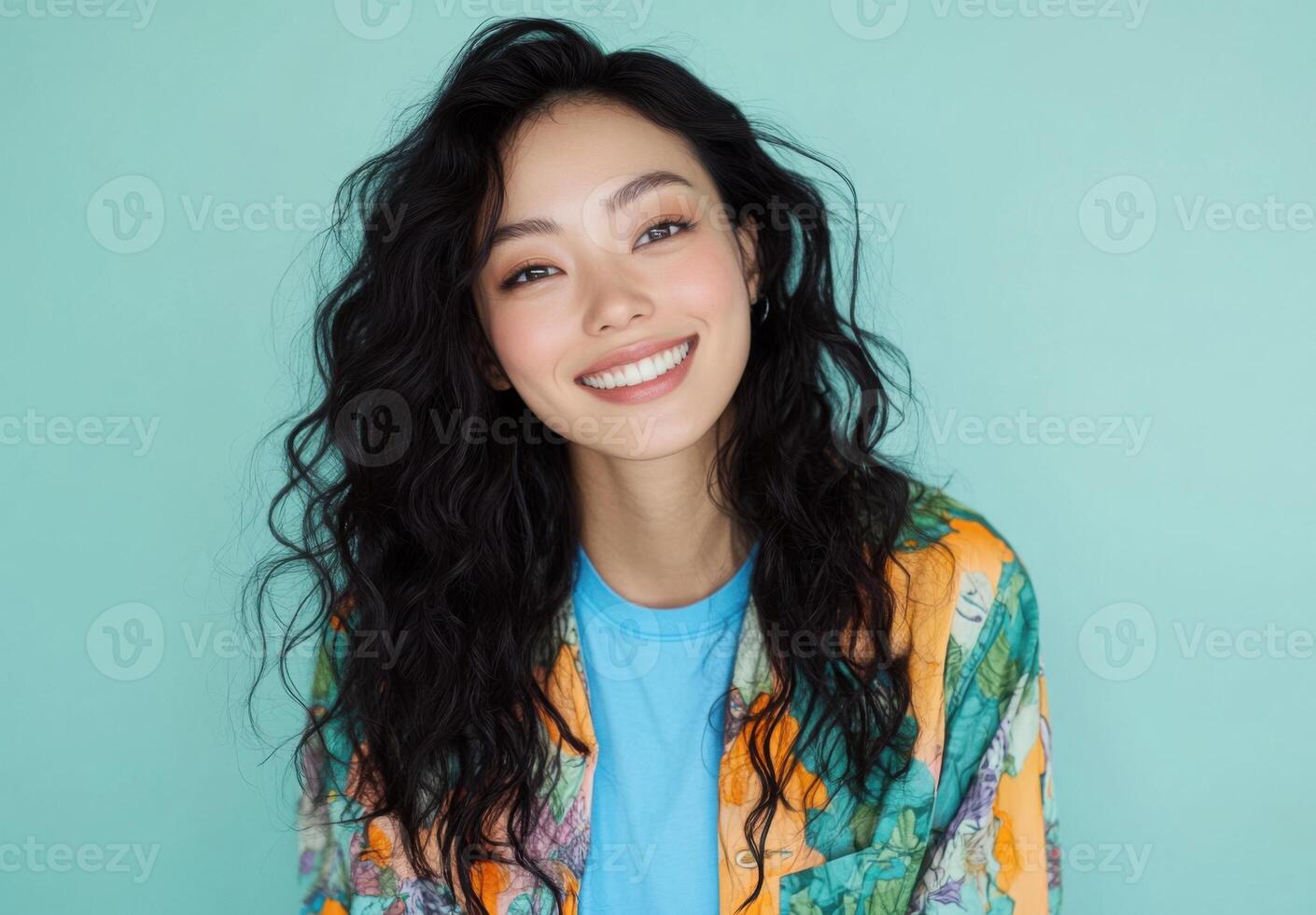 Portrait of a Smiling Young Woman with Long Curly Black Hair, Wearing a Colorful Floral Jacket Against a Teal Background photo