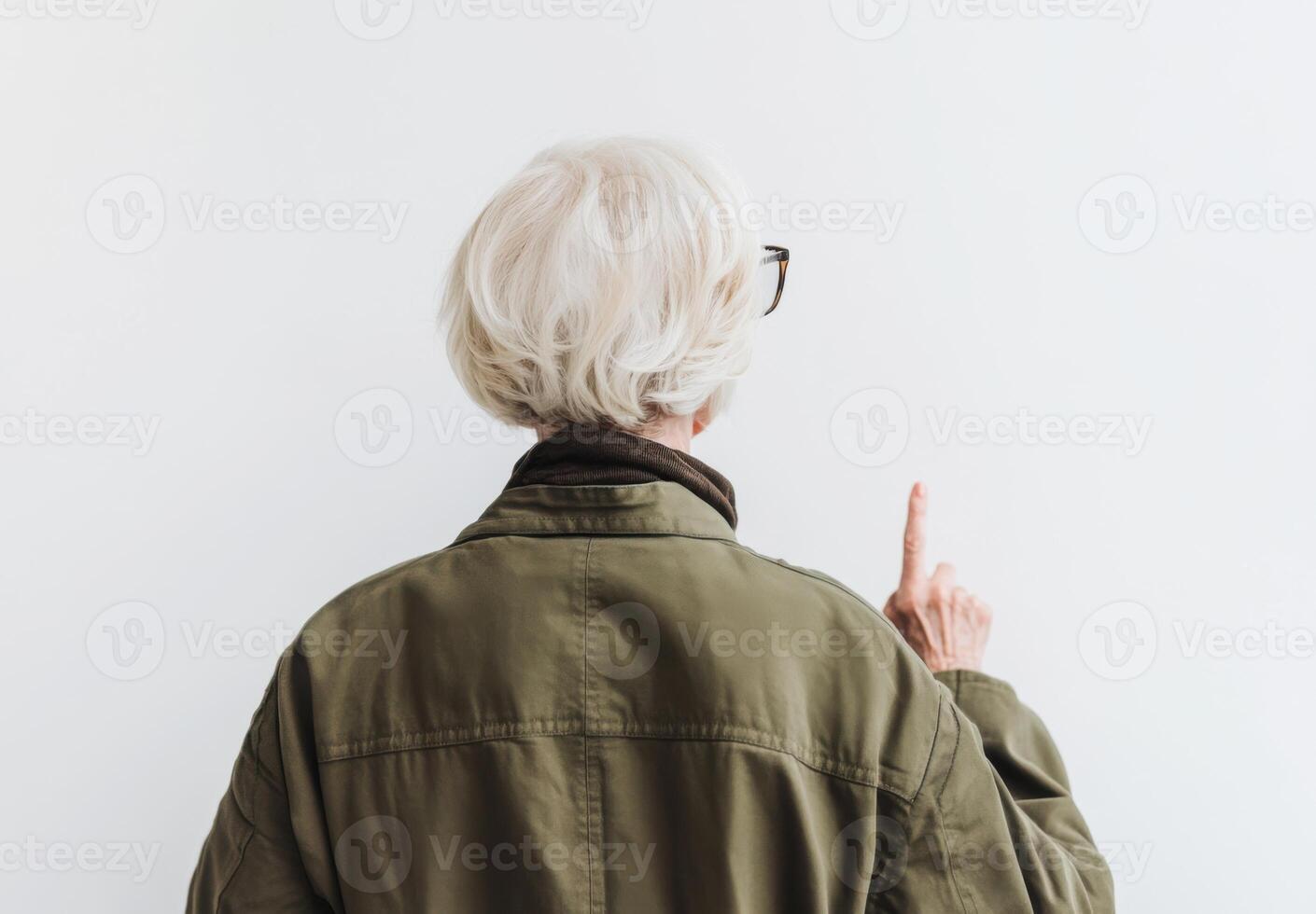 Older Woman Points Upward Against White Wall, Back View photo