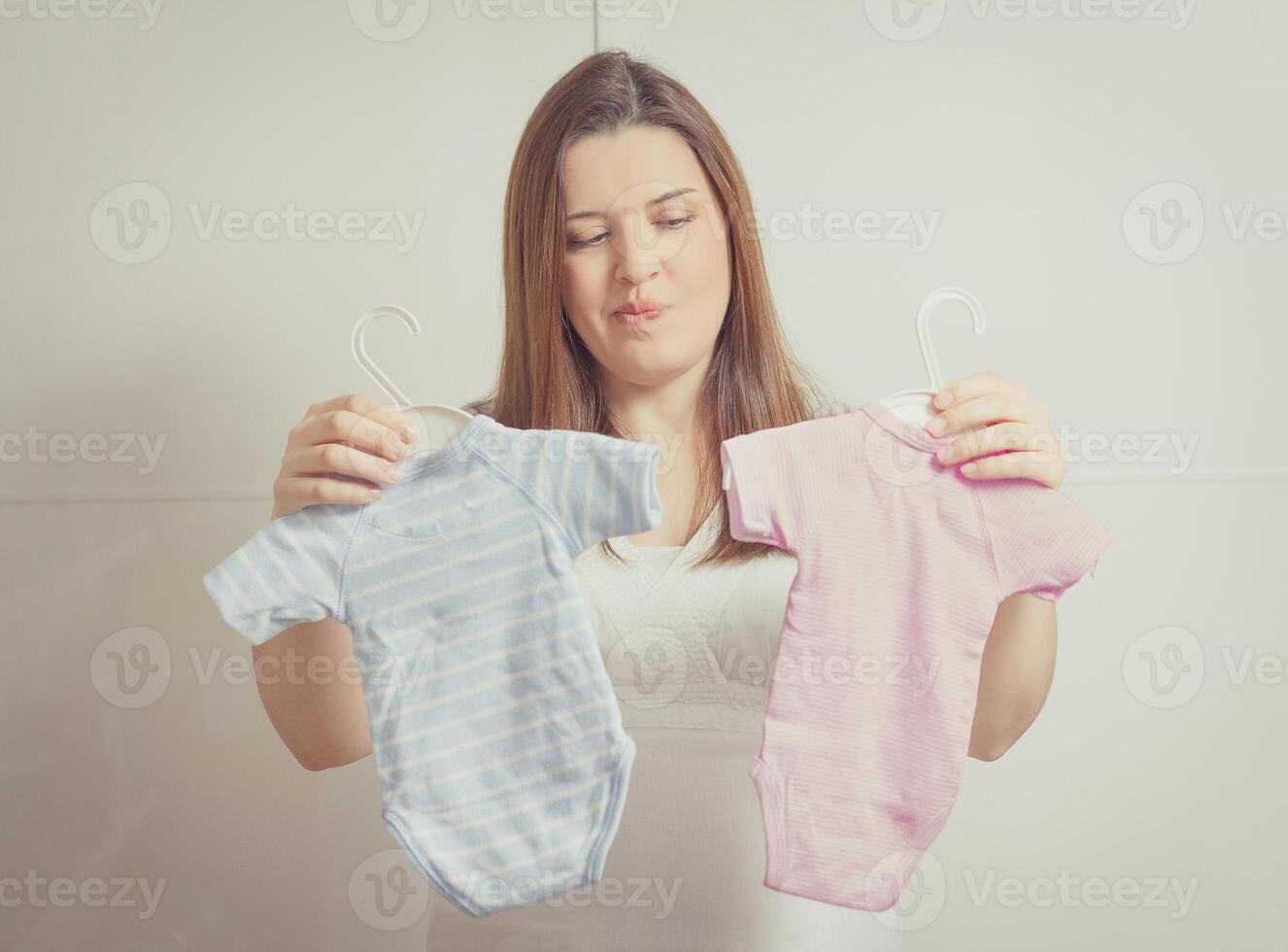 Pregnant woman holding bodysuits for a girl or a boy in soft pastel colors photo