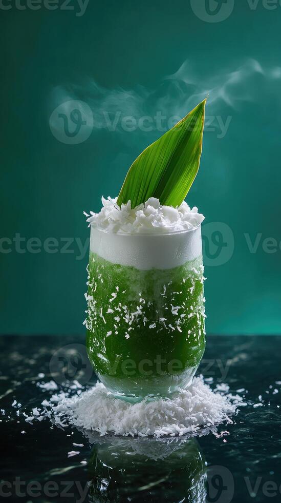 Luxurious pandan coconut milk tea in a tall double-walled glass on a reflective black countertop with teal backdrop photo