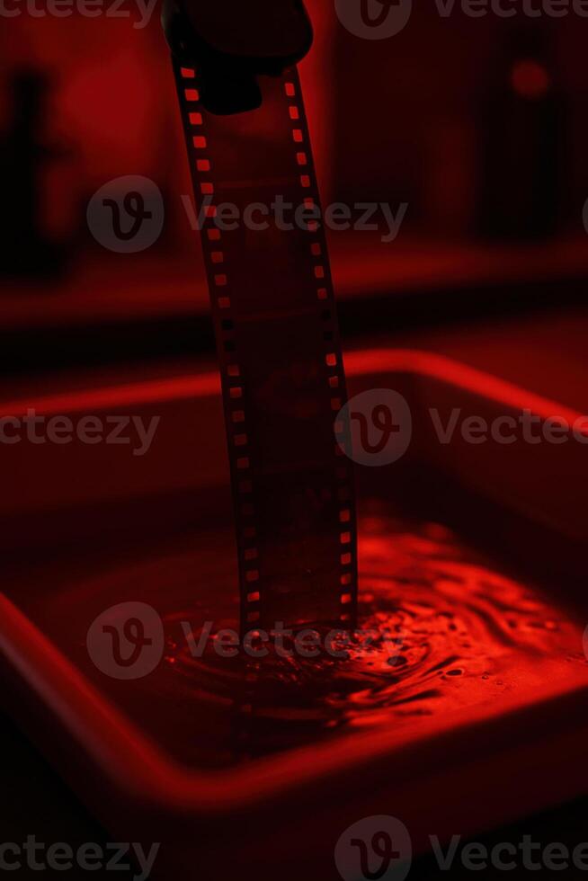 Moody analog film strip developing under red darkroom light photo