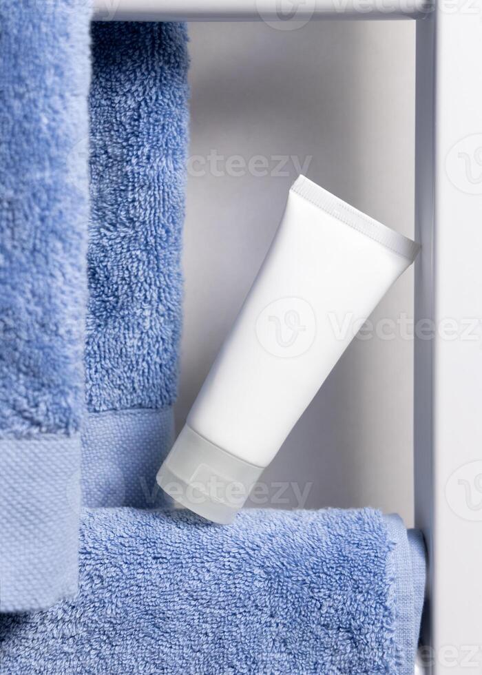 White squeeze cream tube on blue towel on bathroom shelf, closeup, cosmetic mockup photo