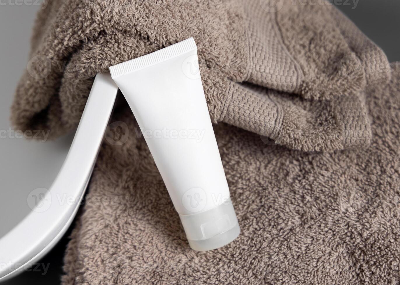 White cream squeeze tube on brown folded towel near vessel basin close up, cosmetic mockup photo
