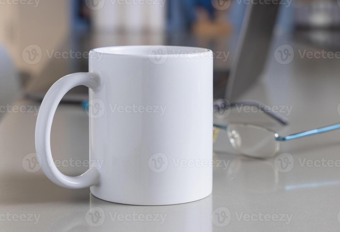White coffee mug on a grey office table against opened laptop and glasses closeup, mockup photo