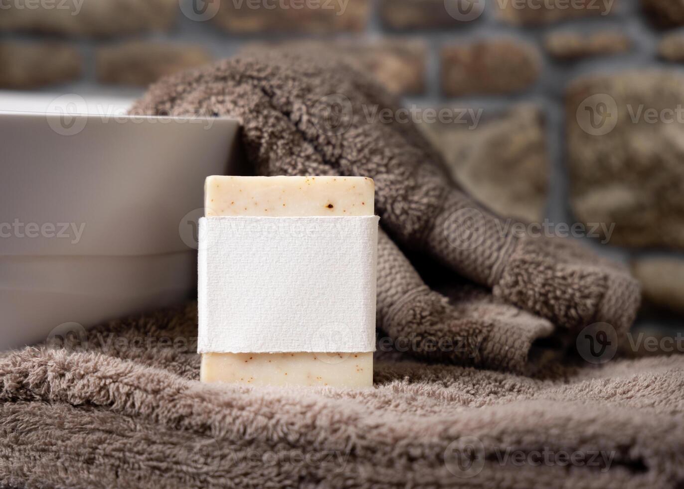 Soap bar with blank label on brown towels near vessel sink against stone wall close up, mockup photo