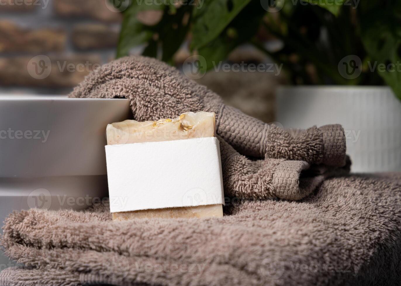 Soap bar with blank label on a brown towels near plant and basin in bathroom, mockup photo