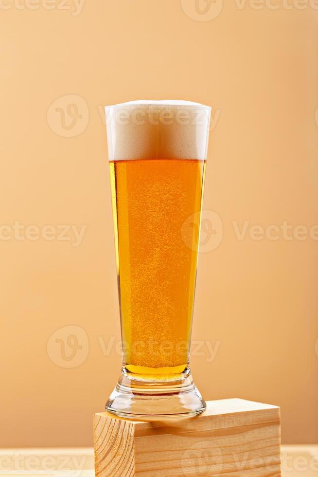 Tall glass of cold golden light beer with foam on top on wooden blocks against warm orange background, showcasing refreshing drink with bubbles. Concept of bar menus, product ads and brewing promotion photo