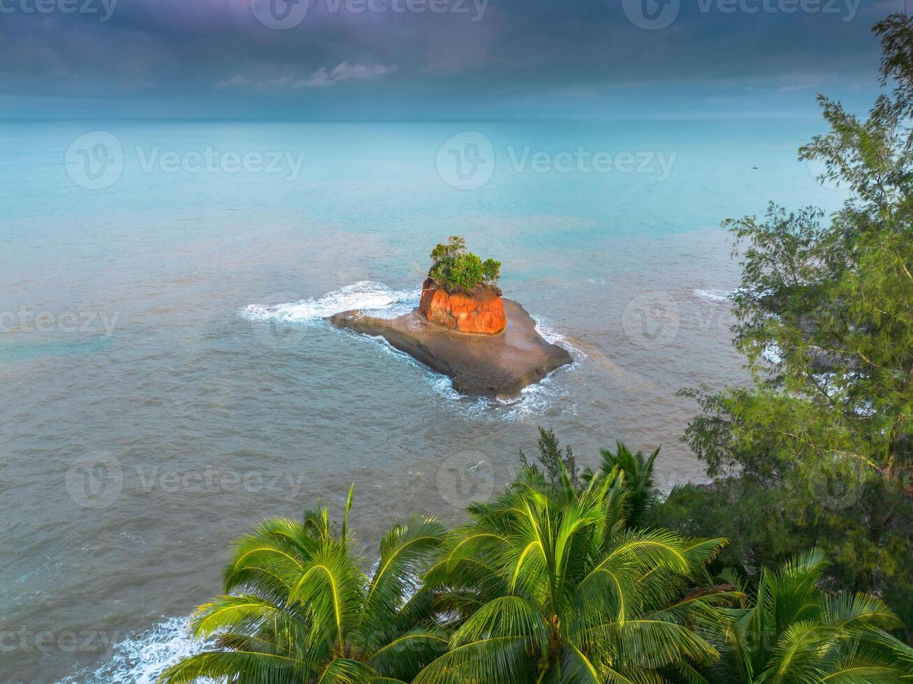 An island in the ocean with a red rock photo