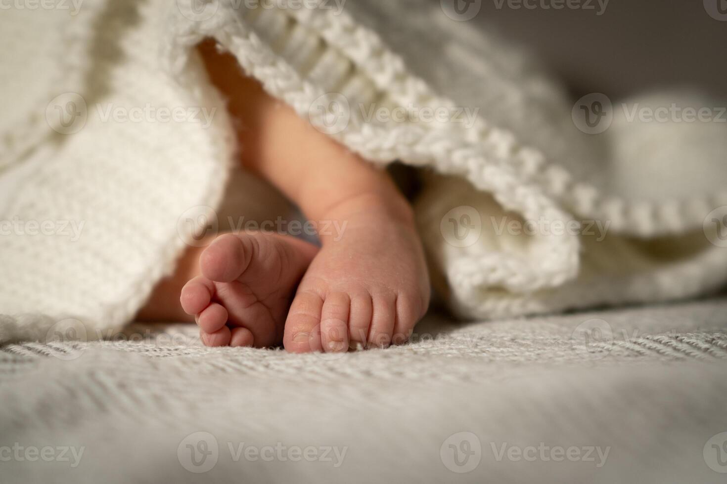Little feet of a baby peeking from under a cozy blanket in a serene nursery during a peaceful afternoon photo