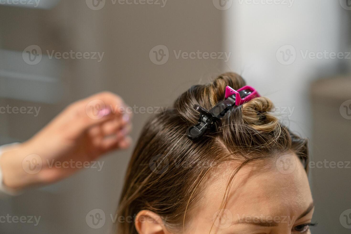 Woman coloring hair in salon with hair clip holding section of hair while stylist works on her photo