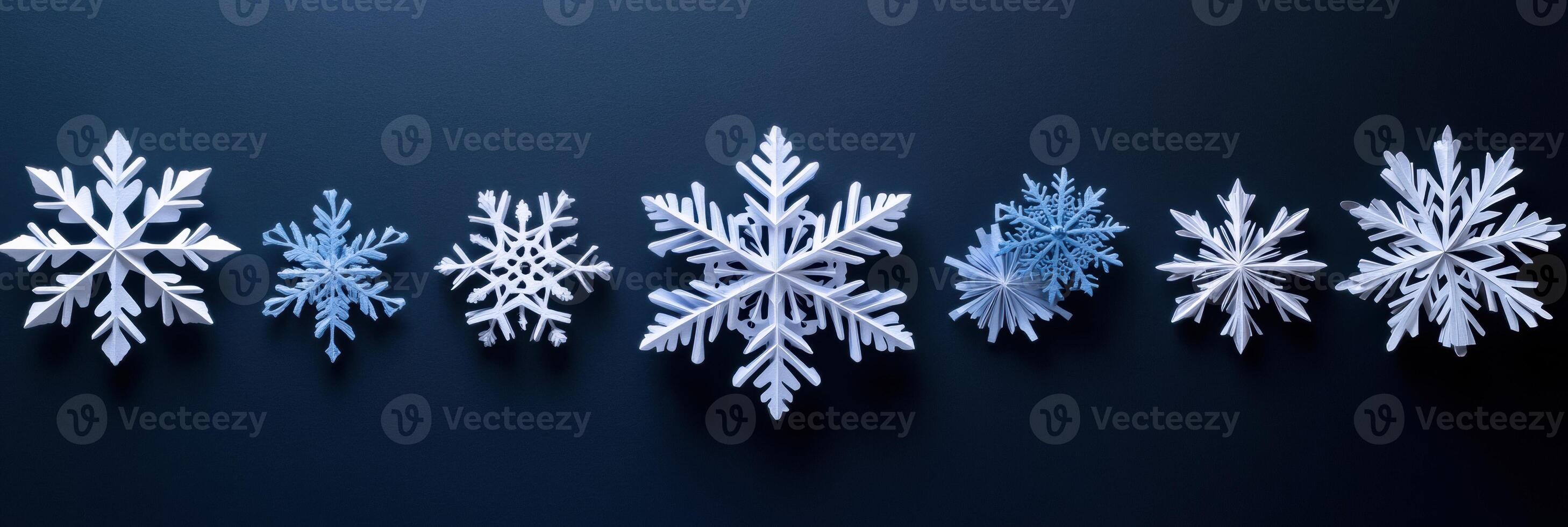 Delicate handcrafted paper snowflakes in various designs rest on a dark surface, offering ample blank space for personal notes or messages. photo