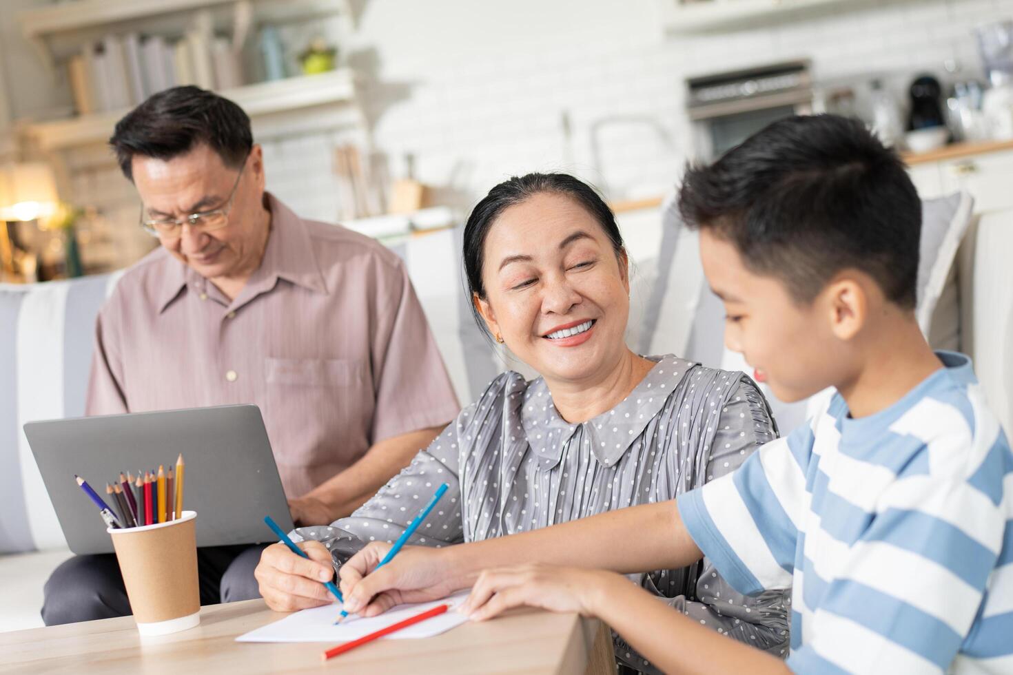 Grandmother helping grandson doing homework while grandfather working with laptop at home. Family spending time on weekend together photo