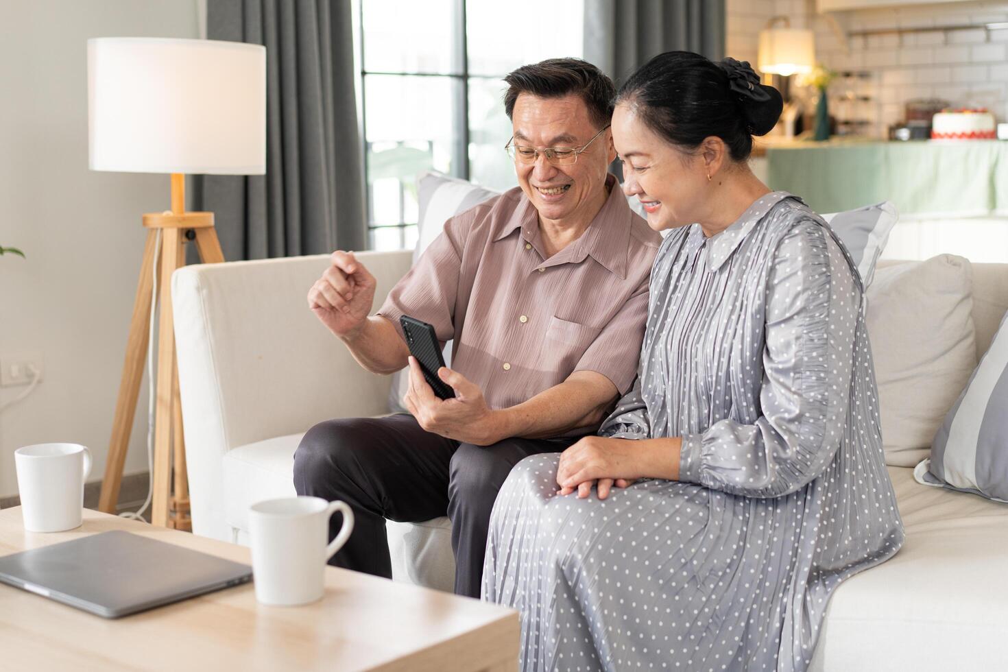 Asian senior couple enjoy using mobile phone on sofa. grandparent learning and connecting with social media, vdo call with family, shopping online, surfing the internet. photo