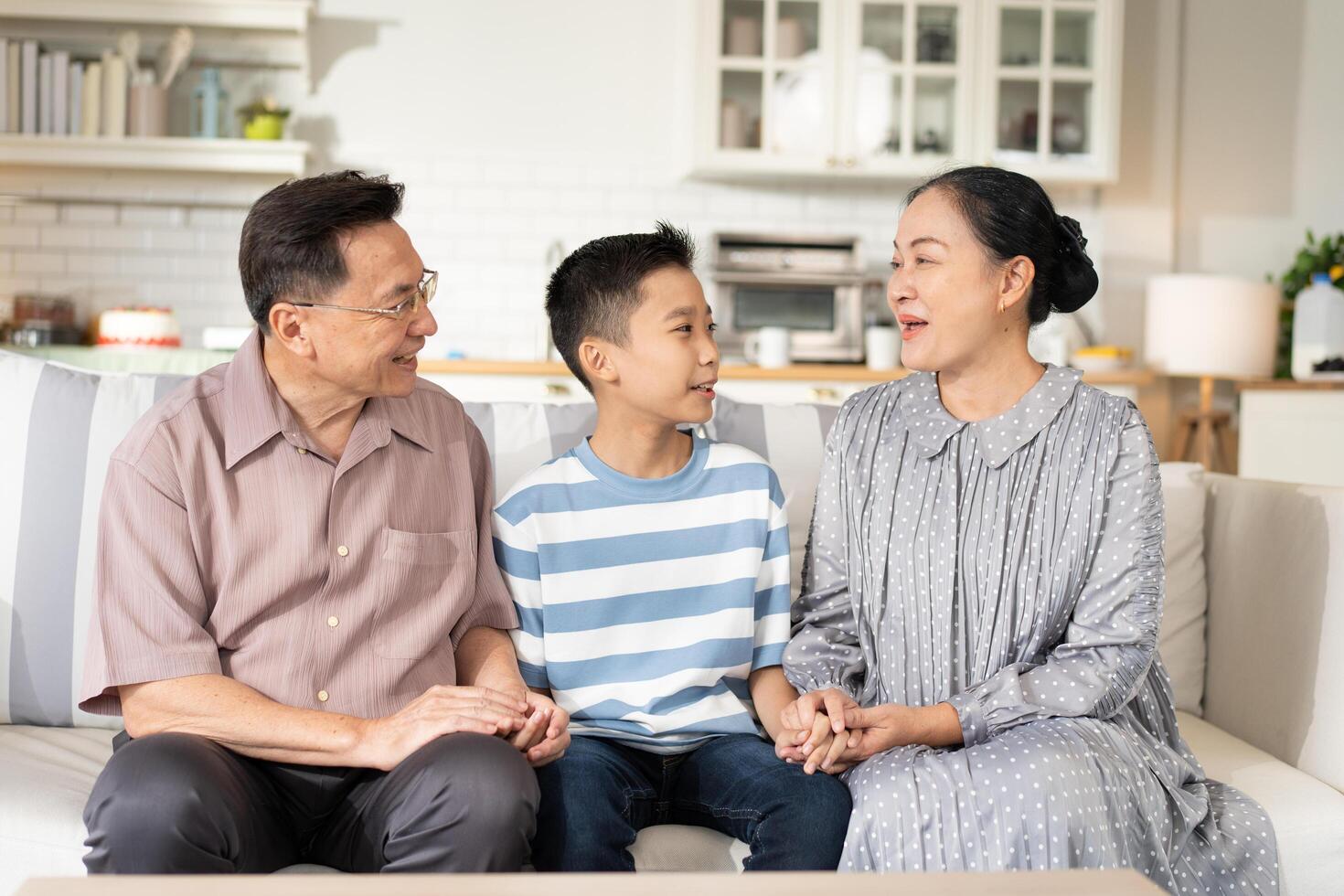 Happy grandson and grandparents relax sitting on couch in the living room looking at camera. Family generation love bonding, people smiling and laughing together at home photo