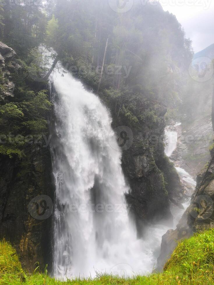 Majestic waterfall cascading through rocky cliffs in a serene forest during a misty morning photo
