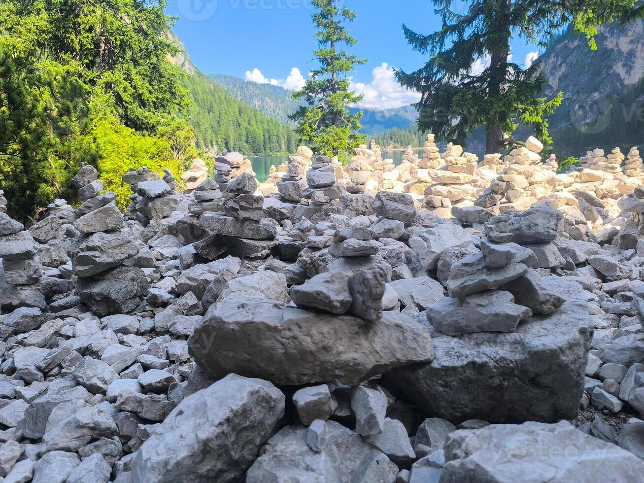 Piles of stones create an artistic landscape along a serene lake in the mountains on a sunny summer day photo
