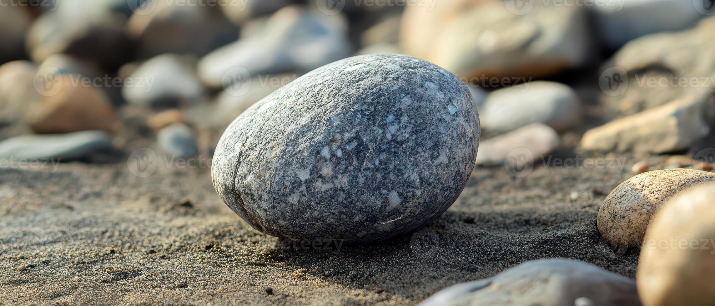 Smooth stone rests on sandy beach by water photo