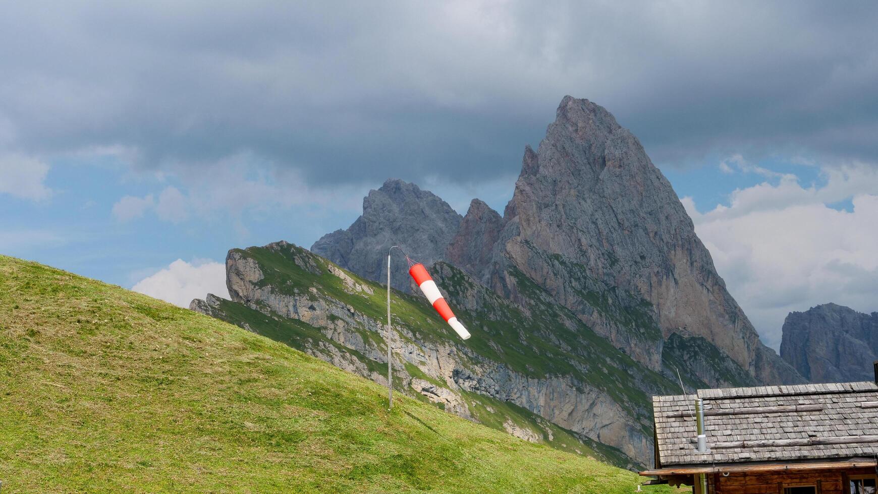 Mountain scenery showcases striking peak against dramatic skies with a windsock fluttering in the breeze during a calm afternoon photo