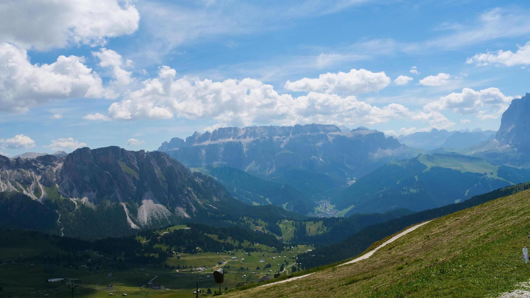 Majestic clouds embrace the Dolomites as sunlight dances over lush valleys and rugged peaks during a crisp summer afternoon photo