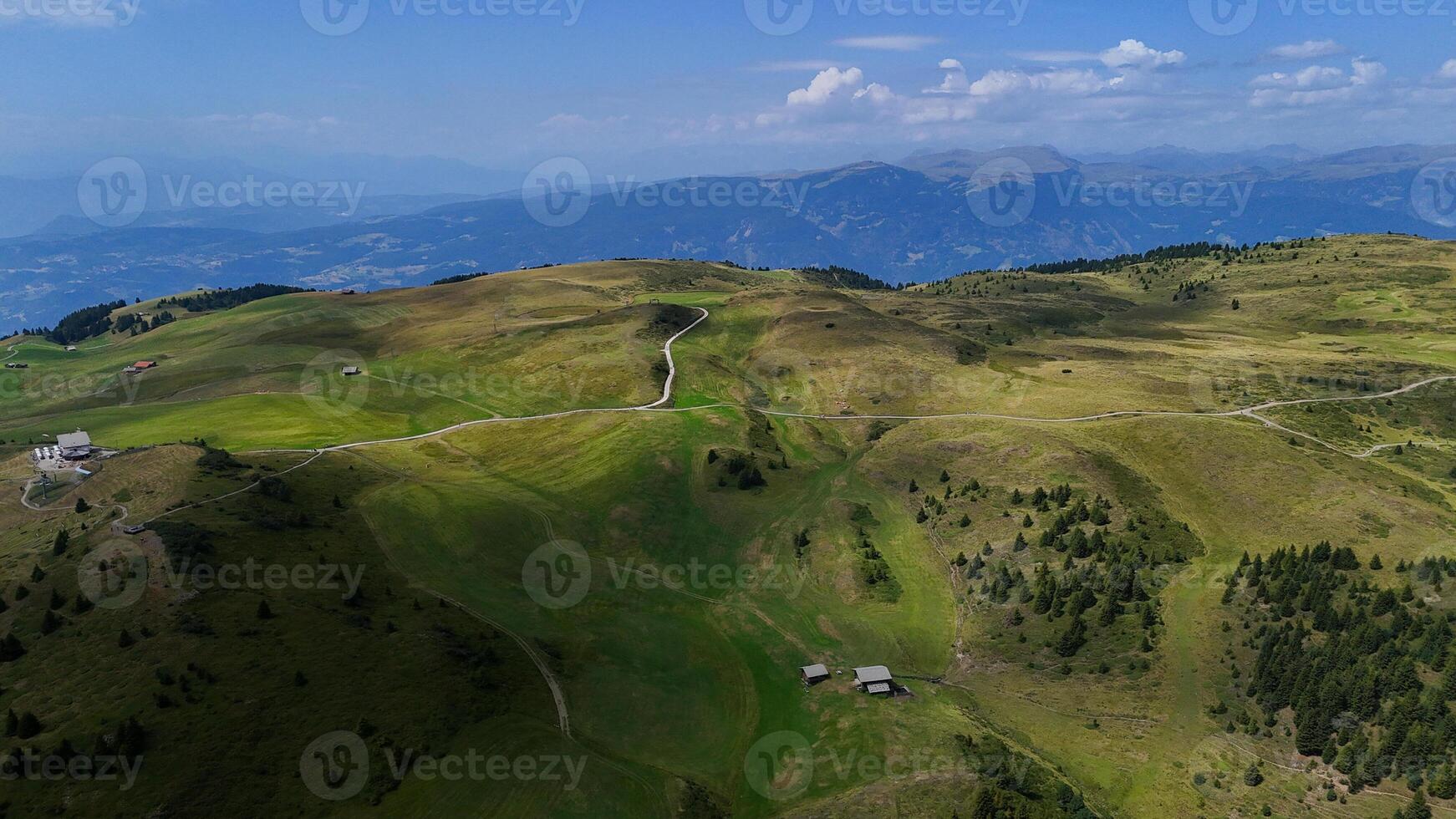 Expansive green meadows stretch across the mountainous landscape under a bright blue sky in a serene midday setting photo