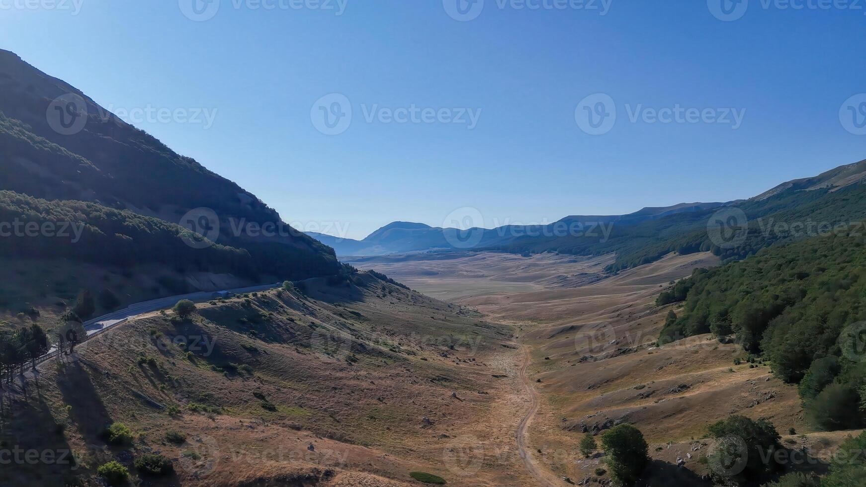 Expansive valley nestled between majestic mountains in the serene countryside under a clear blue sky photo