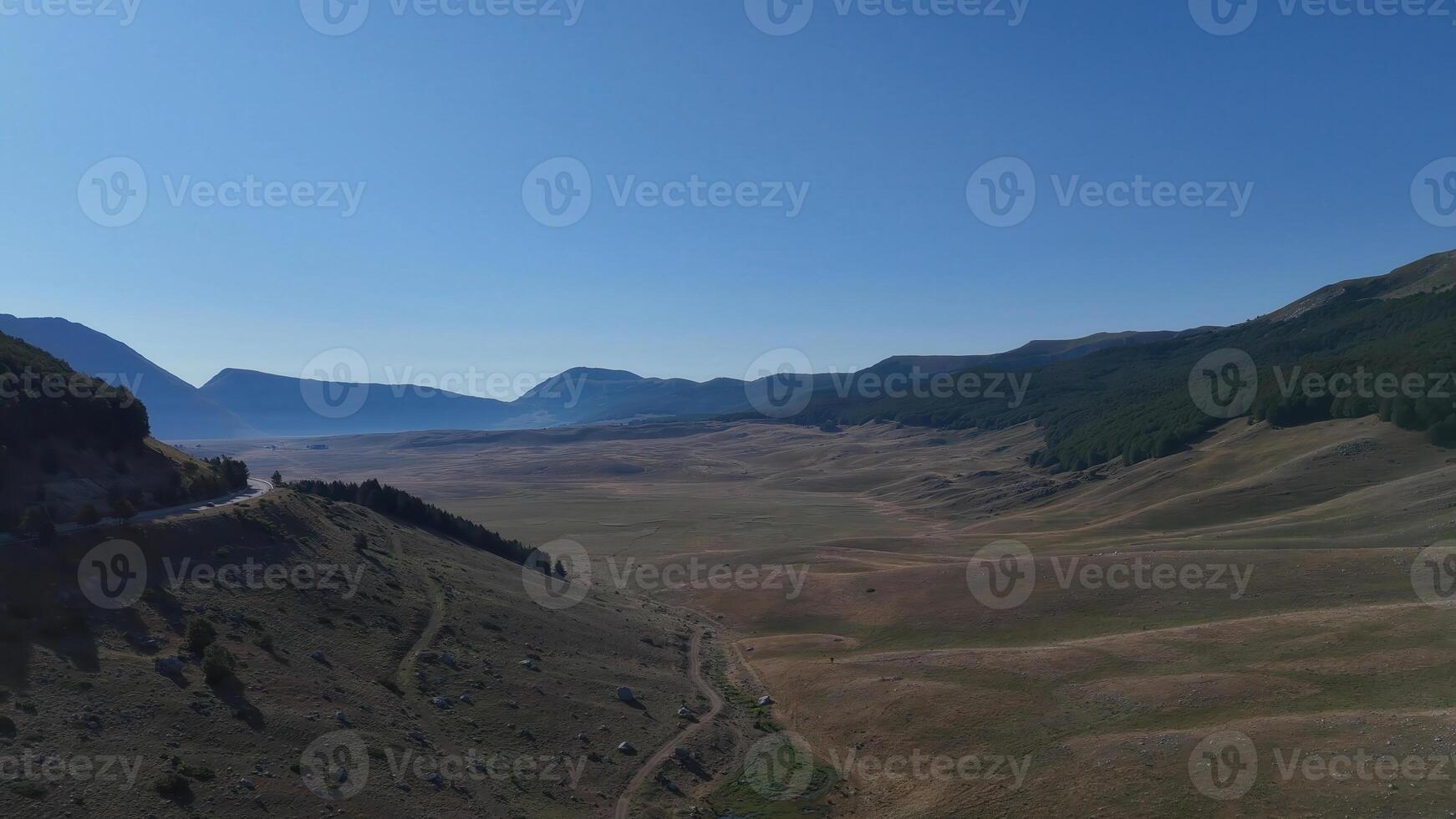 Expansive panoramic view of a serene valley under a bright blue sky in a remote mountainous region photo