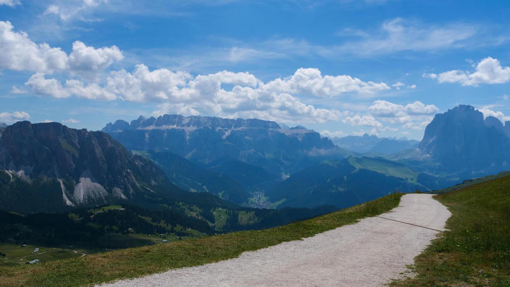 Majestic mountains and open pathway invite adventure in the Dolomites under a bright blue sky filled with fluffy clouds photo