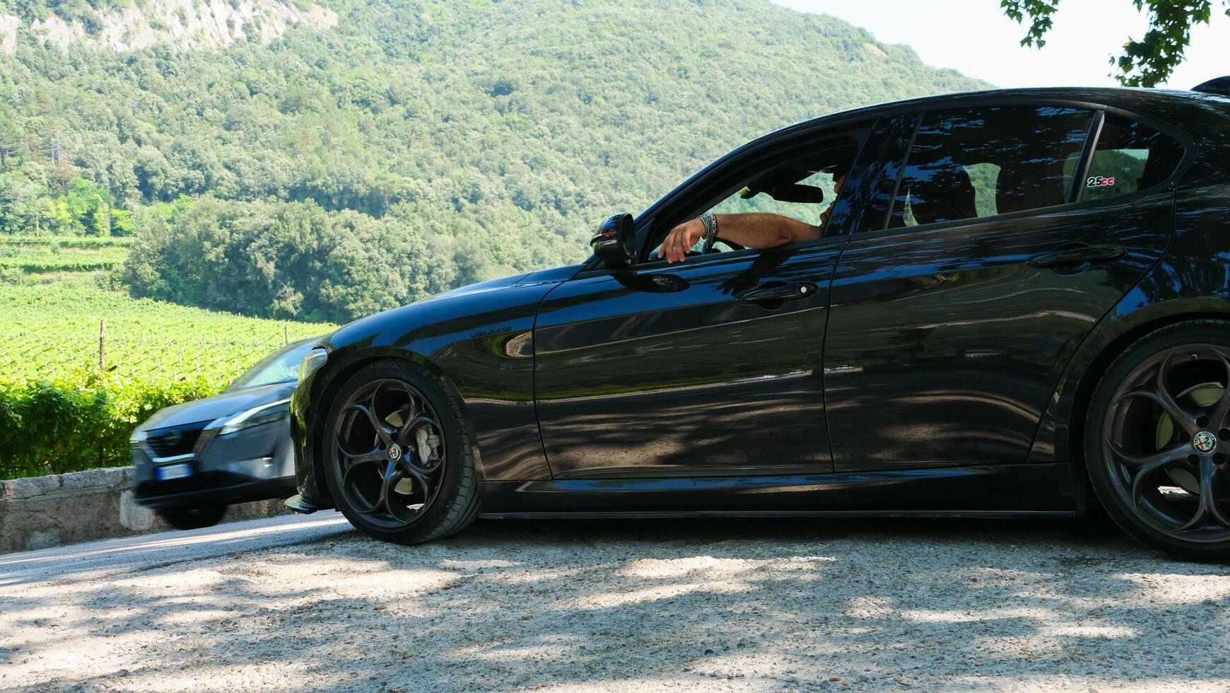 Black luxury car parked along a winding road with vineyard views during a sunny day photo