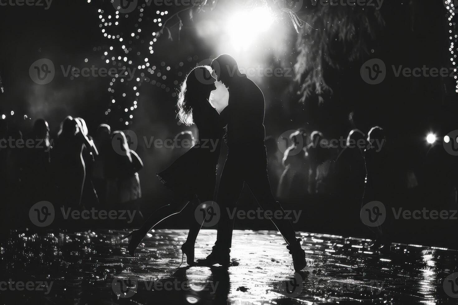 Retro black and white photo of silhouette man and woman dance on a floor outdoor. Dark background with garland.