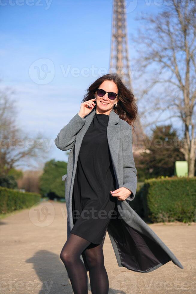 Woman in coat smiling at camera with Eiffel Tower behind photo