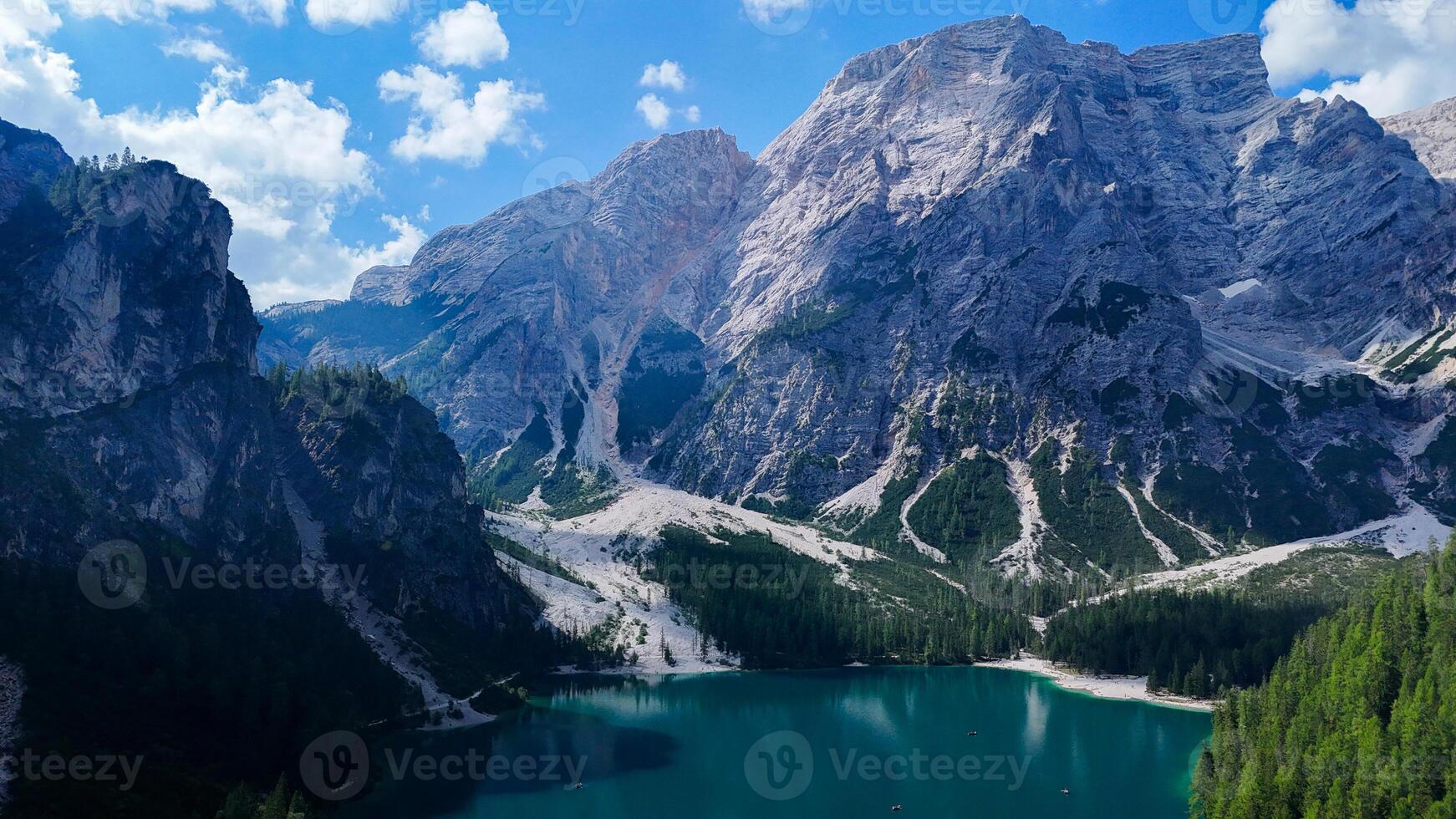 Majestic mountains frame a serene turquoise lake amidst lush forests under a bright summer sky in the Dolomites photo